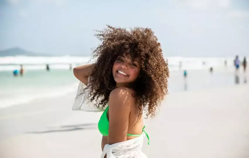 mulher com cabelos afro na praia seguindo dicas para cuidar do cabelo no verão
