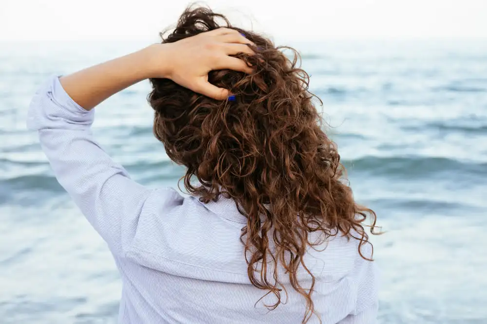 mulher com cabelos cacheados de frente para o mar seguindo dicas para cuidar do cabelo no verão