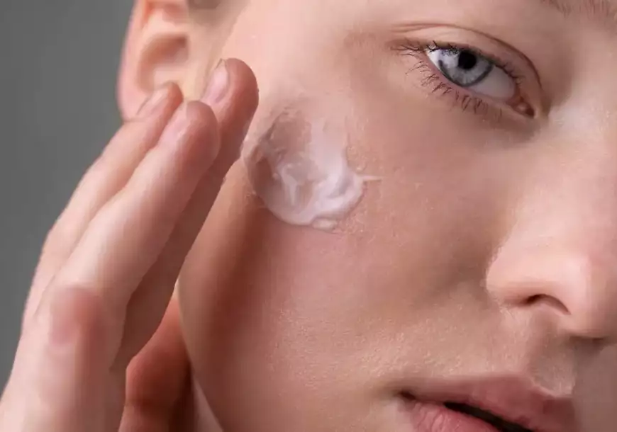 Mulher branca passando creme no rosto pela importância de hidratar a pele diariamente