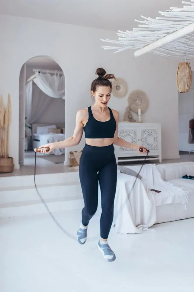 mulher-branca-usando-roupa-de-academia-preta-pulando-corda-faznedo-exercicio-em-casa